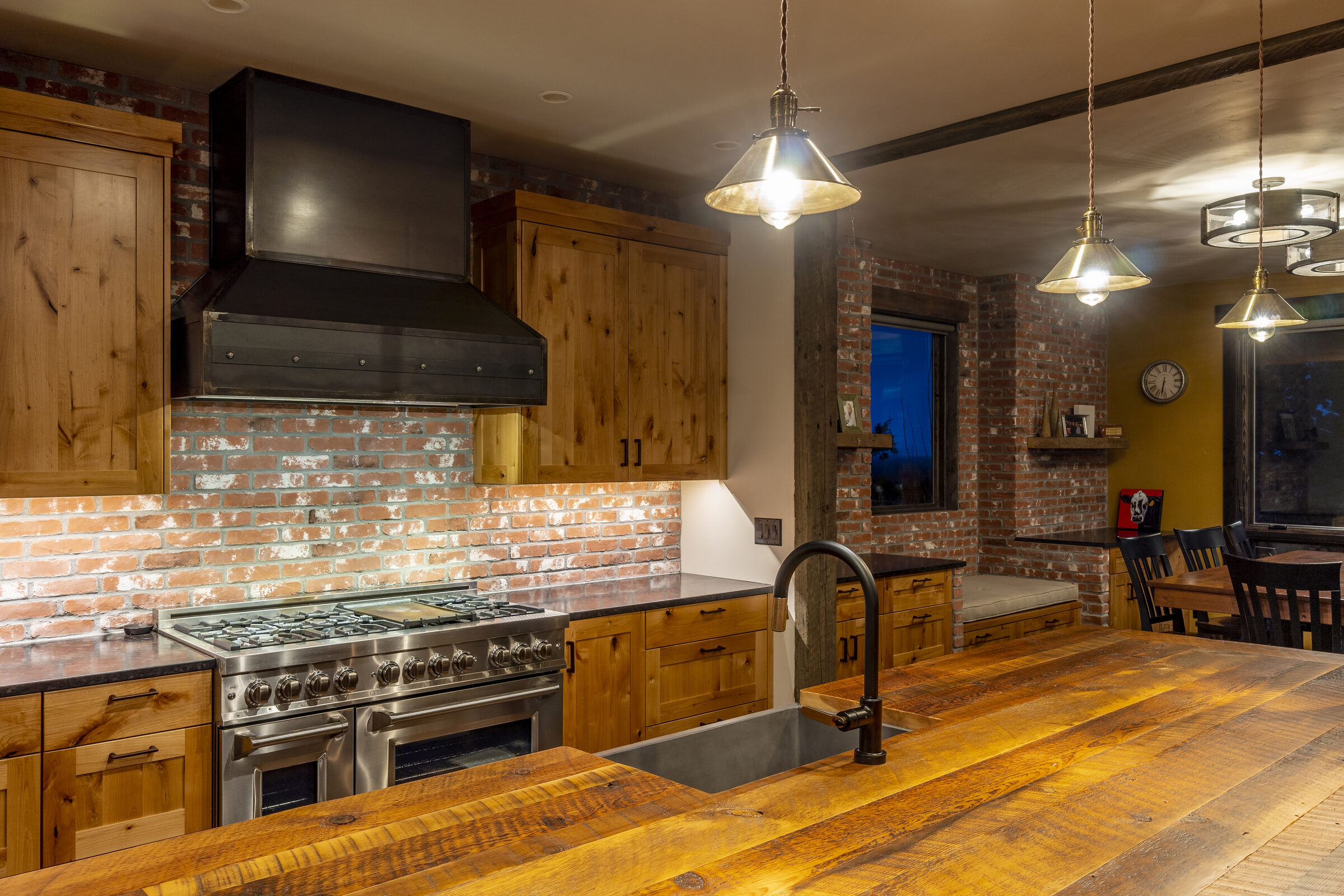 Kitchen with knotty-alder cabinetry, a brick backsplash, and a professional range beneath heavy reclaimed timber