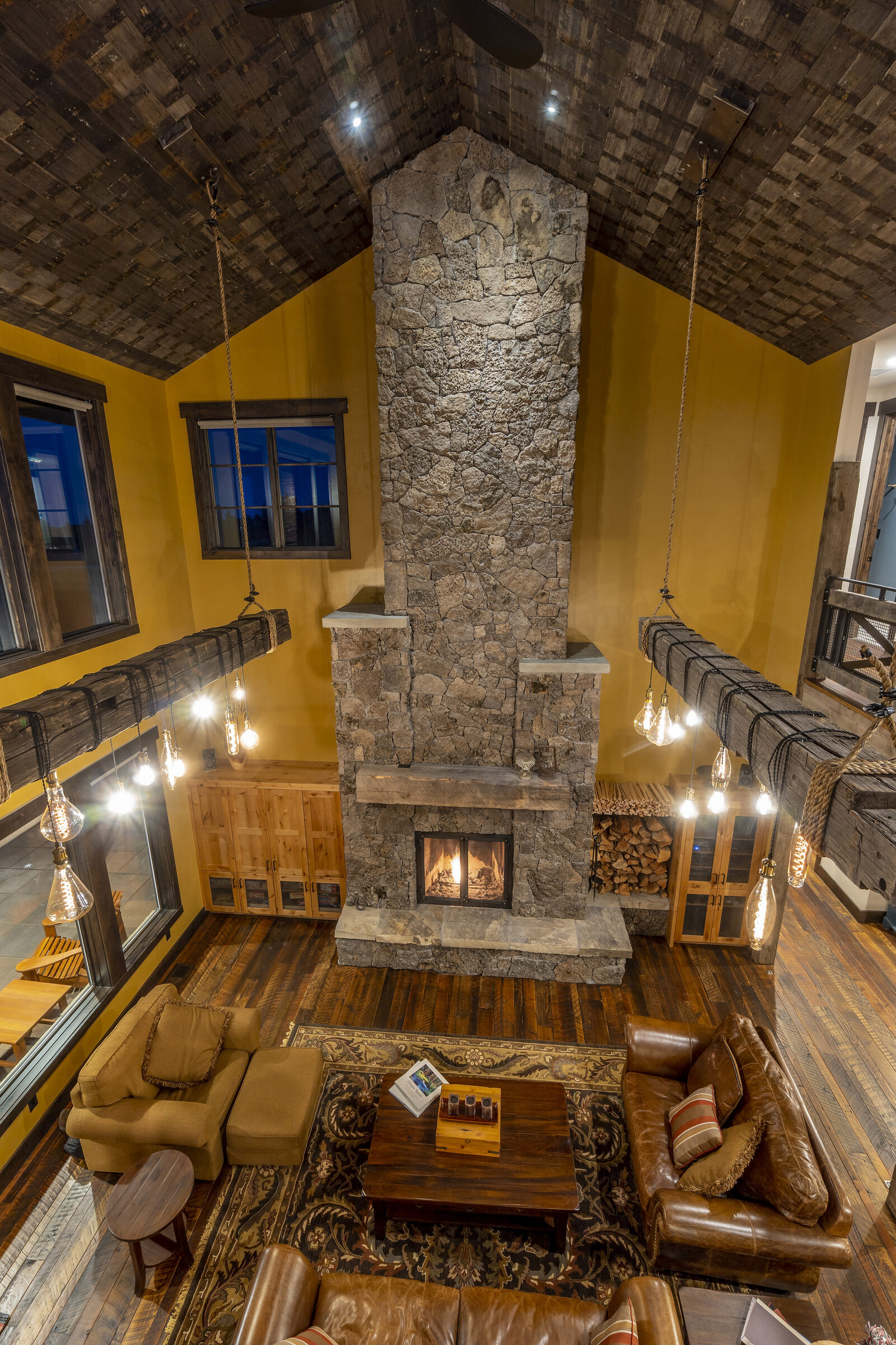 Soaring lava-rock fireplace rising to a vaulted railroad-car-decking ceiling, with hand-hewn antique beams hung on rope as light fixtures