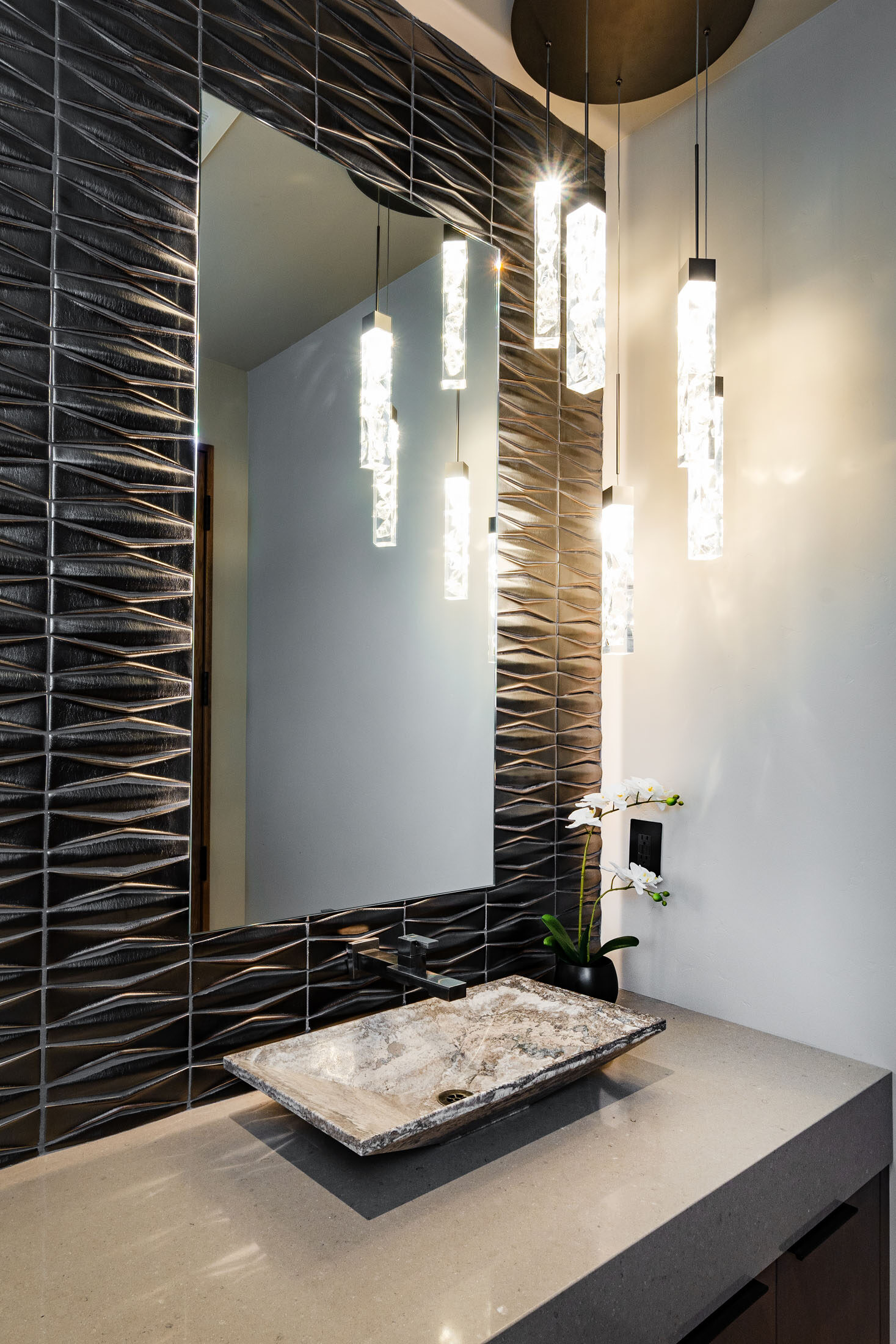 Powder room with textured black tile, a floating stone vessel sink, and pendant lighting