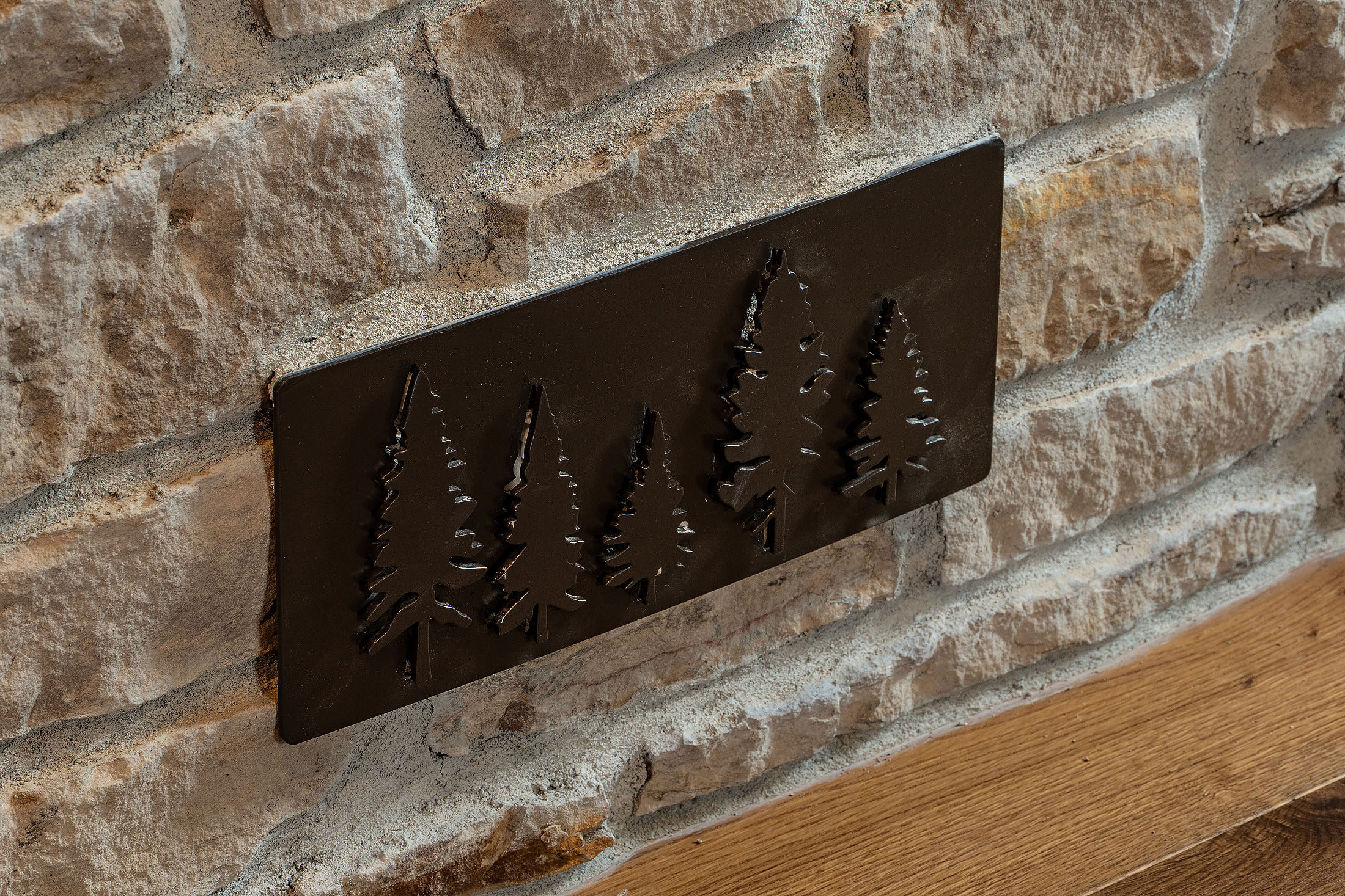 Forged pine-tree art panel mounted on a stacked-stone wall