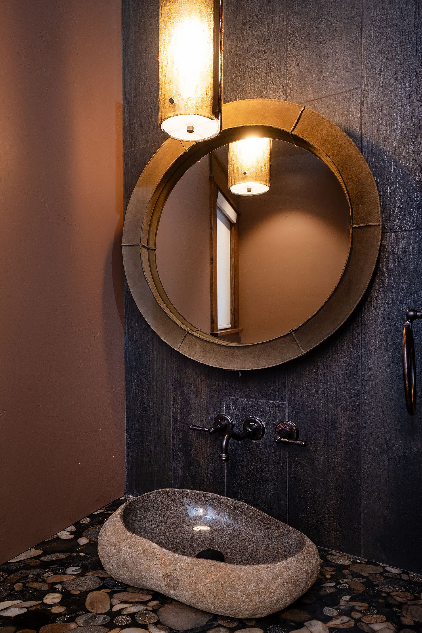 Powder room with a round wood-framed mirror and a stone vessel sink