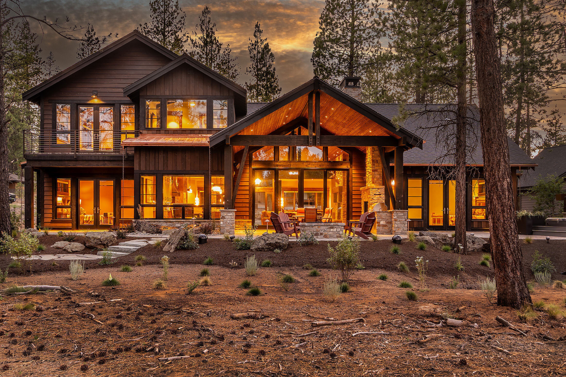 Front elevation at dusk with a timber entry glowing among tall pines, Caldera Springs