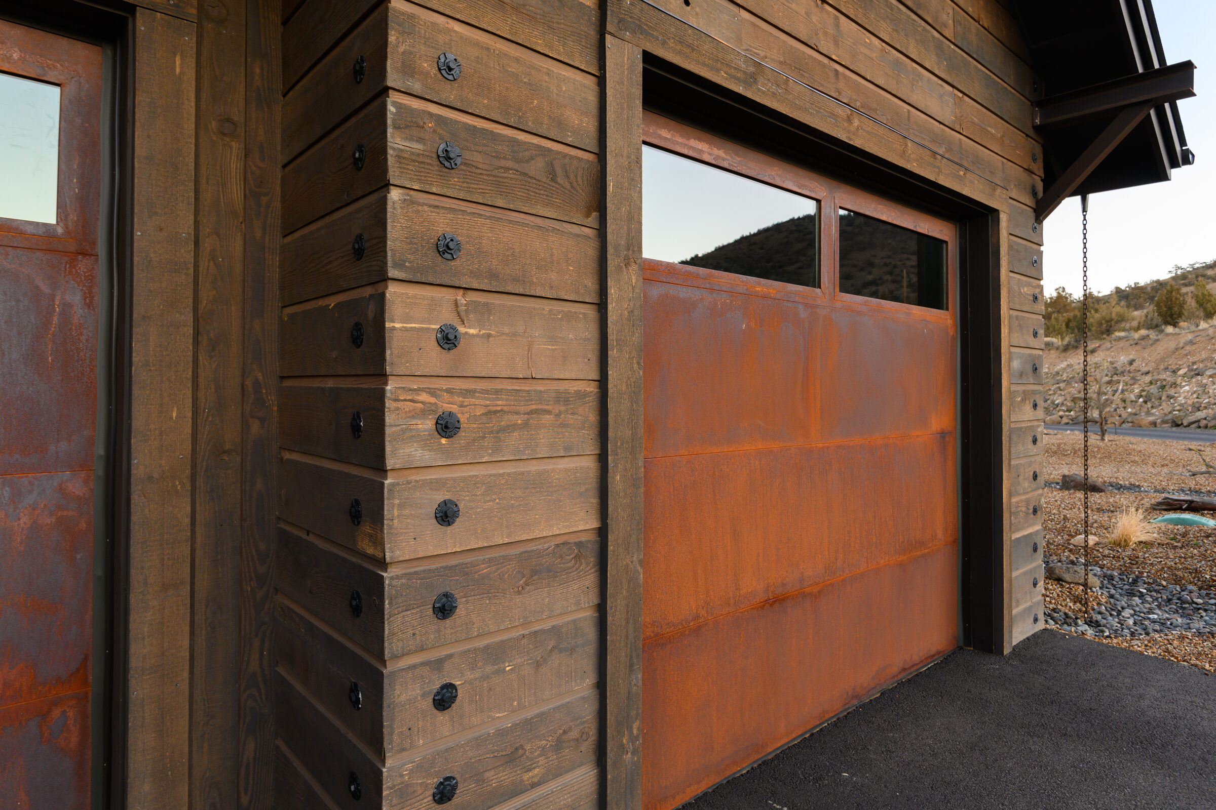 Weathered-steel garage door set into the timber-and-stone exterior