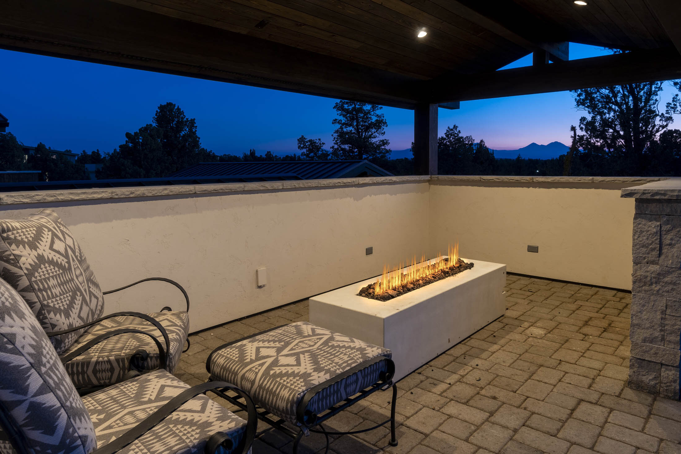 Covered patio with a linear fire table framing high-desert mountain views at dusk