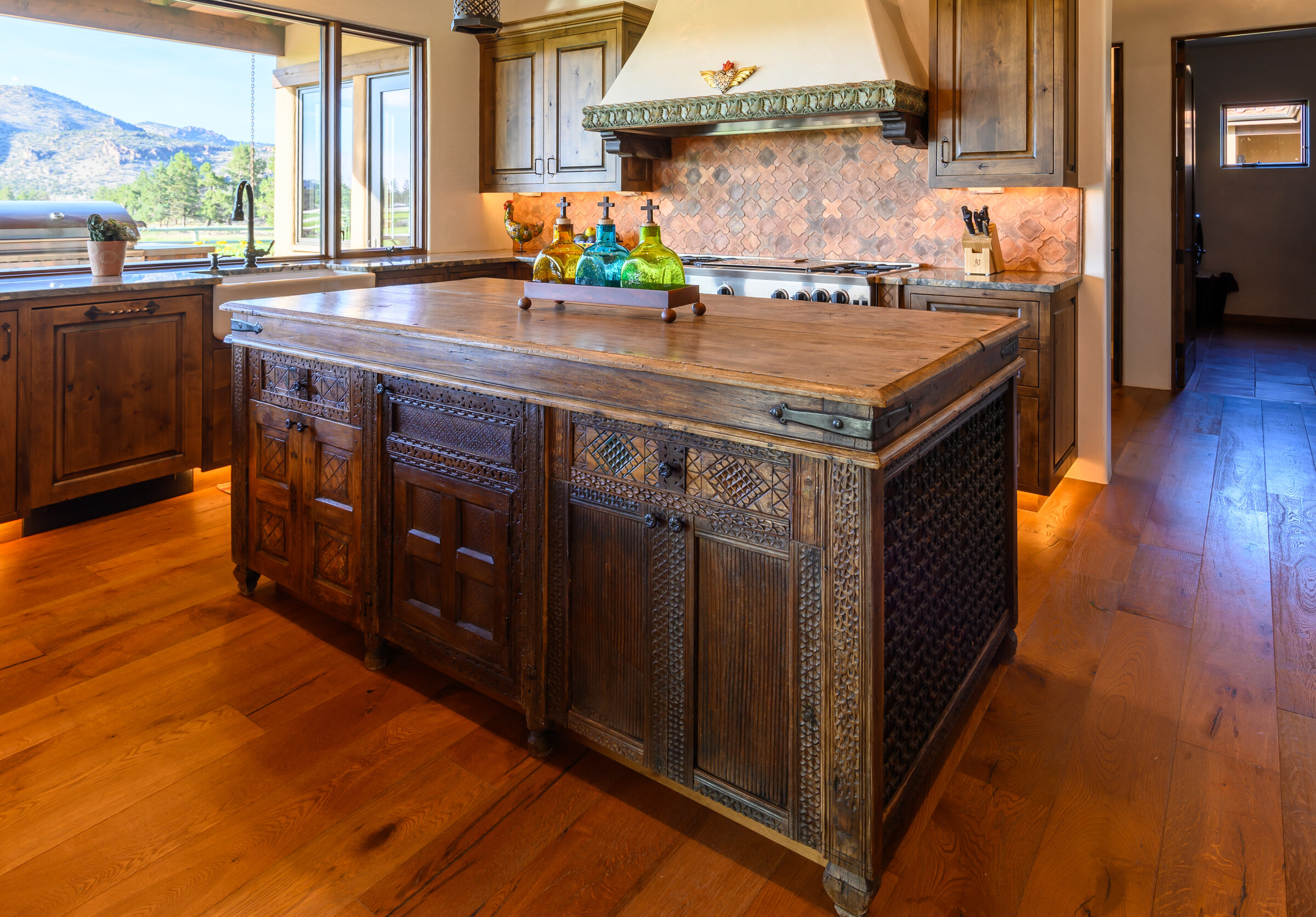 Kitchen island and professional range beneath a carved-wood hood