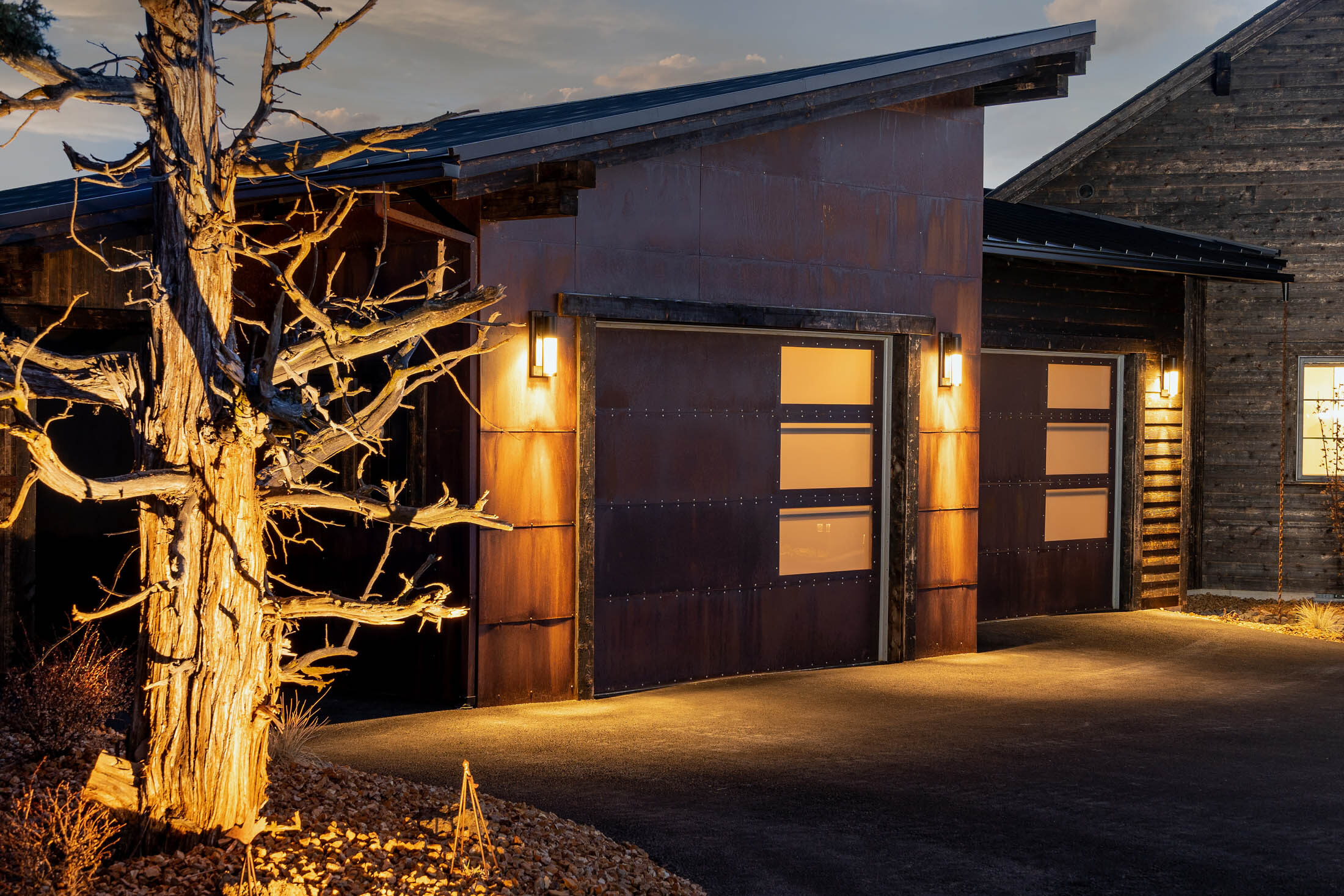 Wildhorse bronze-clad garage and old-growth juniper glowing at dusk, Brasada Ranch