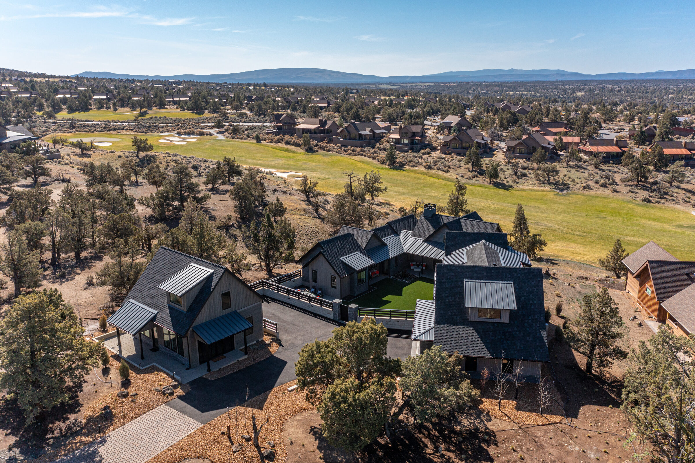 Aerial of the modern home and its turf courtyard set into the high-desert golf community, with the Cascades beyond