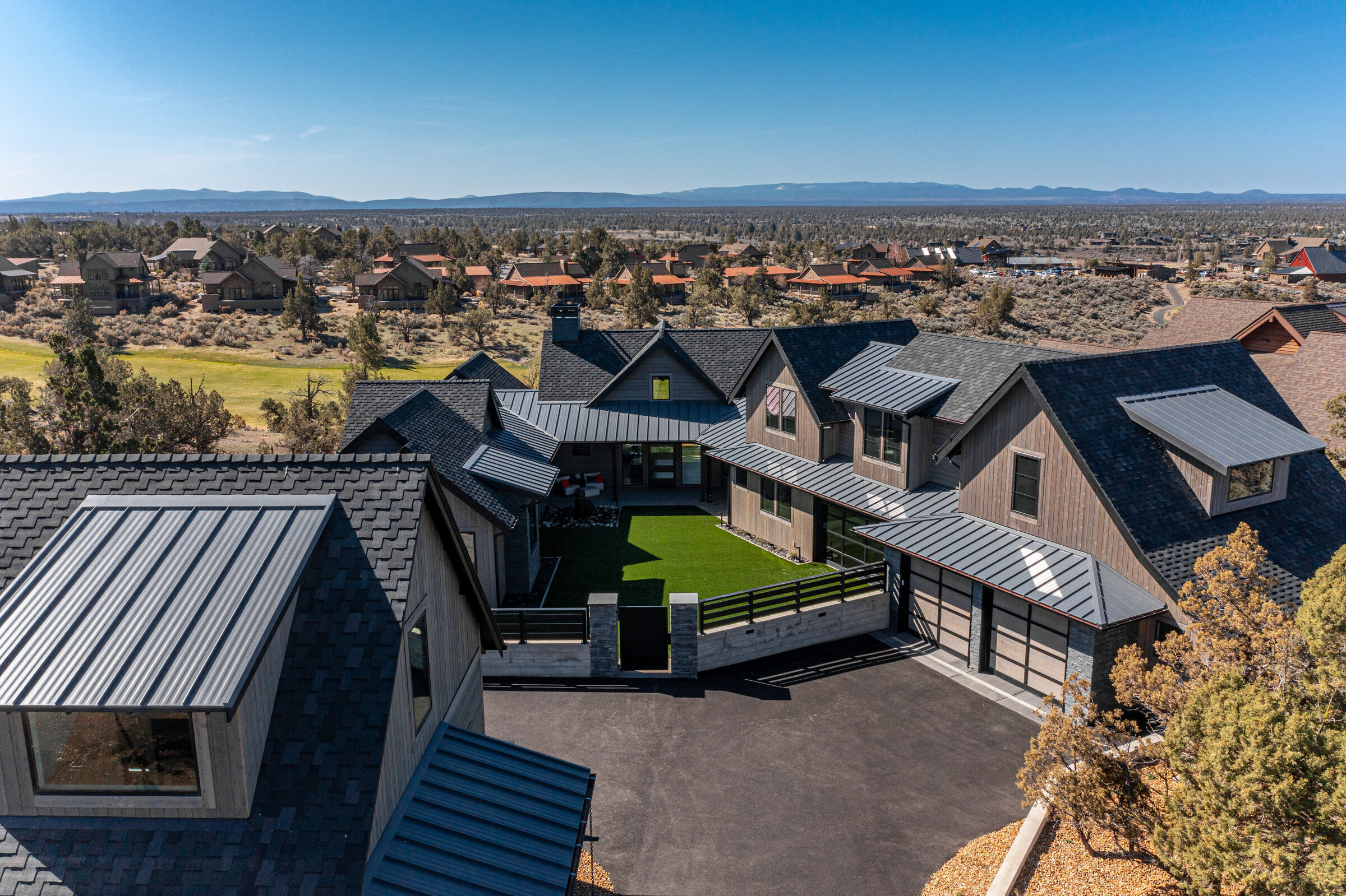 Aerial of the modern home wrapping a central turf courtyard, with the golf community and Cascades beyond, Wooden Trestle at Brasada Ranch